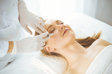 Obraz na płótnie Canvas Beautician doctor doing beauty procedure with syringe to blonde female face. Cosmetic medicine, beauty injections concept
