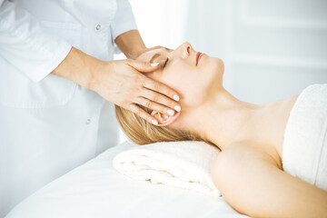 Beautiful happy woman enjoying facial massage with closed eyes in spa salon. Relaxing treatment in medicine and Beauty concept