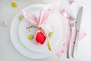 top view of easter egg wrapped in pink napkin shaped like bunny ears