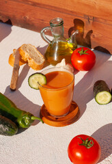 concepto de un vaso de gazpacho  en una mesa blanca con todos los ingredientes para hacer el gazpacho andaluz alrrededor del vaso.
