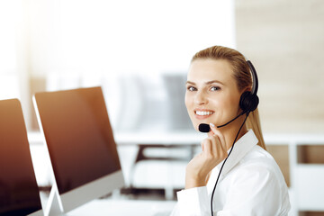 Blond female customer service representative is consulting clients online using headset in sunny...
