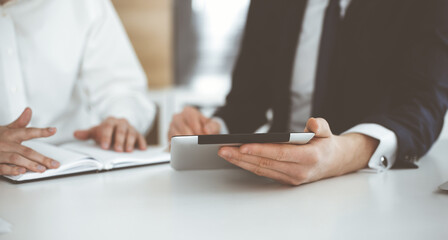 Unknown business people using tablet computer in modern office. Businessman or male entrepreneur is working with his colleague at the desk