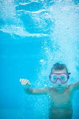Naklejka premium Cute little boy in a swimming pool, diving, swimming underwater, having fun