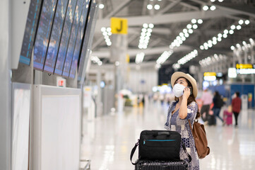 Asian tourist woman wear face mask checking time table of flight and talking with mobile phone at the airport during coronavirus or covid-19 outbreak pandemic situation.