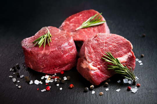 Raw beef filet mignon steaks with rosemary, pepper and salt on dark rustic board