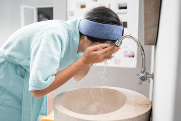 a woman wearing a towel clean her face with water in the sink in the bathroom