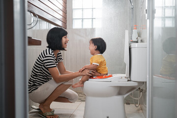 a woman help her daughter to sit on the toilet while poop at bathroom