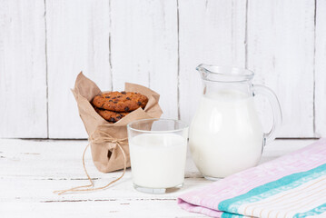 Delicious cookies with chocolate, a glass cup and a jug of milk on a wooden white table. Beautiful...