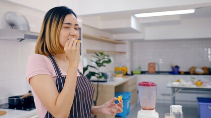 Portrait Asian young happy beautiful Woman eating spoon of fruit smoothie in the kitchen. female emotion making a very sour expression. Healthy lifestyle concept.