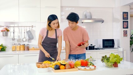 Happy Asian couple enjoy with cooking in Kitchen. Loving couple feed each other while cooking together in modern kitchen enjoy conversation and healthy vegetarian salad food preparation.