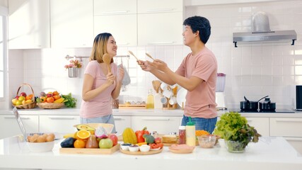 Happy Asian couple dancing laughing together preparing food at home, carefree joyful husband and wife having fun cooking healthy romantic dinner meal listen to music in modern kitchen