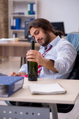 Young male employee drinking alcohol in the office