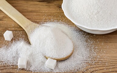 Bowl and wooden spoon with white granulated sugar and sugar cubes on a wooden background. Close up.