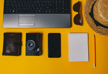 Fototapeta na wymiar accessories for work with travel on the beach: laptop, wallet, straw hat, notepad, telephone, vintage camera, pen, sunglasses on a yellow background top view