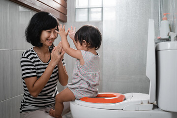baby poop clapping jokingly with his mother against the background of the toilet in the bathroom