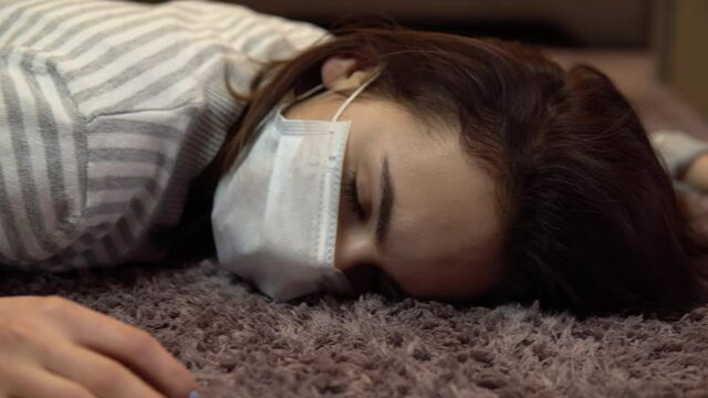 A young woman lies on the floor dead. A woman in a medical mask lies on the floor of unconsciousness closeup.