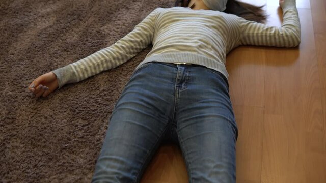 A young woman lies on the floor dead. A woman in a medical mask lies on the floor of unconsciousness. View from above.