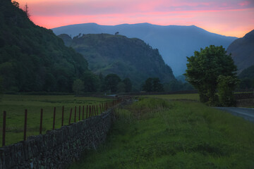 Colourful sunset or sunrise sky over a country road and old stone wall in English countryside landscape near Grasmere in the Lake District, Cumbria, England.