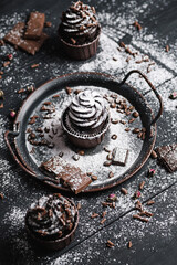 Several muffins or cupcakes with chocolate shaped cream at black table. Powdered sugar is scattered over the cakes