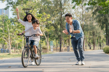 Obraz premium Happy Asian family father and mother teaching their son to ride bicycle at the park