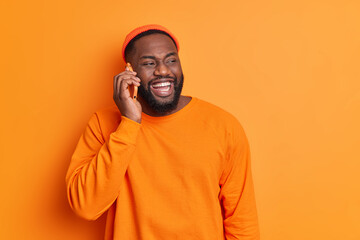 Pleasant conversation concept. Cheerful bearded dark skinned guy makes phone call smiles broadly...
