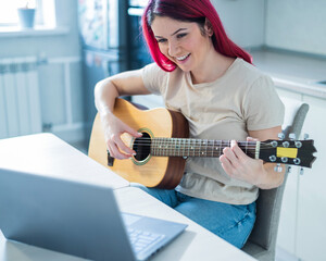 A woman sits in the kitchen during a remote acoustic guitar lesson. A girl learns to play the...