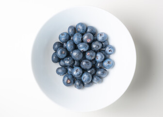 Overhead view of superfood antioxidant blueberries in a white bowl on a plain white surface and background.