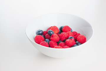 Superfood mixed berries of raspberries and blueberries in a white bowl on a plain white surface and background.
