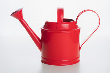 A shiny red indoor watering can on a plain white surface and background.