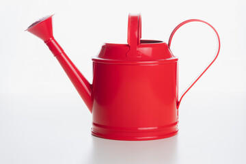 A shiny red indoor watering can on a plain white surface and background. © Stephen