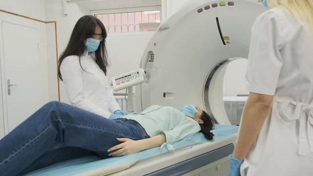 Two radiologists inserts an intravenous catheter to inject contrast to female patient who is undergoing CT or MRI scan. Patient lying on a CT or MRI scan bed, moving inside the machine.