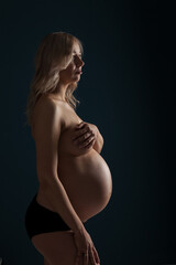 Silhouettes of a pregnant beautiful woman naked topless and covering her breast with a big belly in anticipation of the birth of a child.