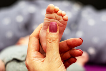 Der winzige Fuß eines neugeborenen Babys im Vergleich zum Daumen der Mutter
