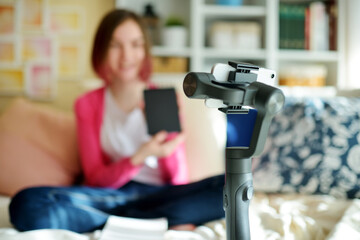 Beautiful teenage girl recording video blog with her smartphone. Young vlogger shooting vlog at home. Teen influencer creating content for her social media account.