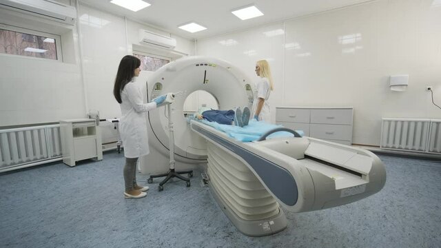 Female patient is undergoing CT or MRI scan under supervision of two qualified radiologists in modern medical clinic. Patient lying on a CT or MRI scan table, leaves the machine