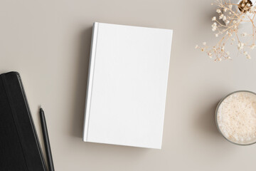 White book mockup with a gypsophila, coffee and workspace accessories on the beige table.