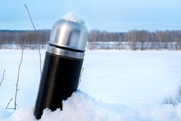 Iron thermos in snow against the icy river on a sunny day. Winter travel