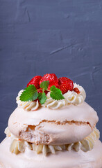 Tall Pavlova cake with whipped cream and strawberry against the gray background. Multilayered meringue dessert
