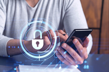 A programmer is browsing the Internet in smart phone to protect a cyber security from hacker attacks and save clients confidential data. Padlock Hologram icons over the typing hands.