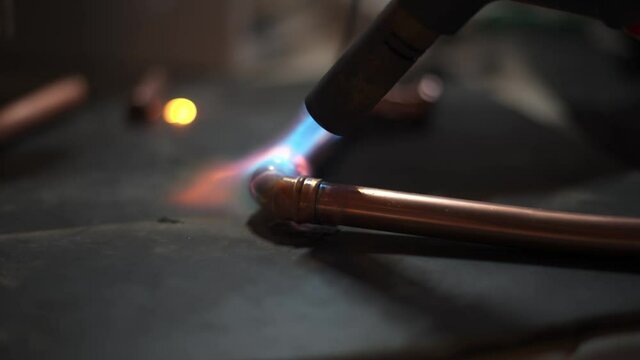 Flame from a gas blowtorch being applied to a copper pipe fitting, to melt solder and seal the joint.