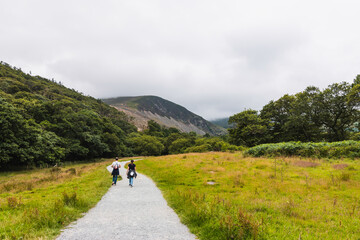 Fototapeta na wymiar two people on their backs walking along a path in the direction of a mountain in a natural green landscape