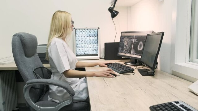 Professional female doctor radiologist examines brain CT or MRI scan results, working on a computer screen at her personal desk at hospital