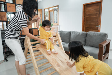 a woman patiently holding a baby while standing sliding on a pikler triangle toy at home