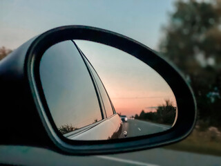 The car's rear-view mirror shows a view of the road and the cars behind on the highway. Auto travel concept.