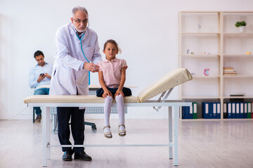 Small girl with her father visiting old male doctor