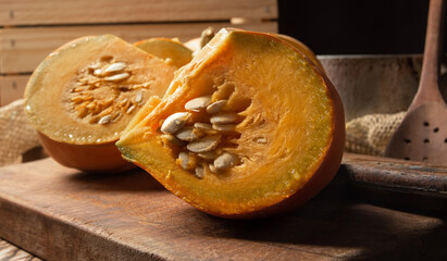 Pumpkin, rustic arrangement with pumpkin cut into pieces, knife, board, wooden spoon, iron pot on a table, with rustic fabric and wood, black background, selective focus.