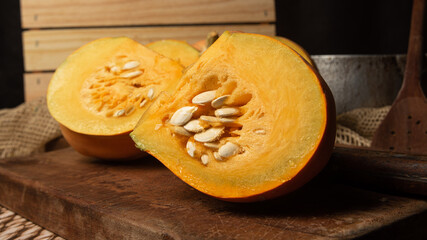 Pumpkin, rustic arrangement with pumpkin cut into pieces, knife, board, wooden spoon, iron pot on a table, with rustic fabric and wood, black background, selective focus.
