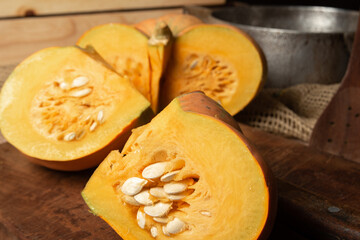 Pumpkin, rustic arrangement with pumpkin cut into pieces, knife, board, wooden spoon, iron pot on a table, with rustic fabric and wood, black background, selective focus.