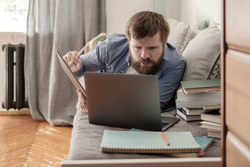 Student lies on a couch, looks intently at a laptop. Concept of distance online education.