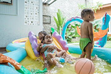 siblings and friends playing together sliding down on rubber pool at home